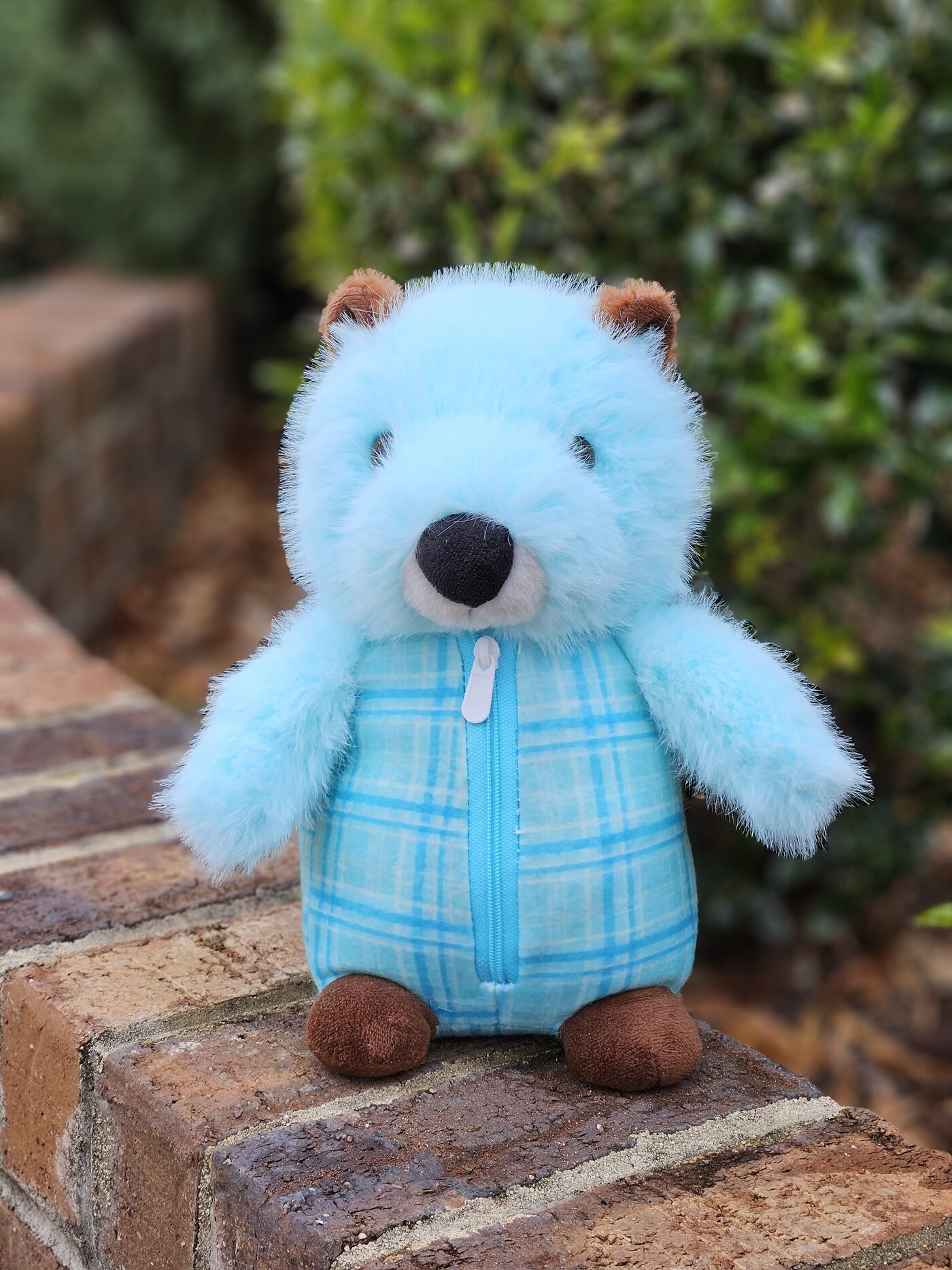 The Grounding Groundhog, a soft blue weighted plush with brown ears and paws, sitting on a brick wall